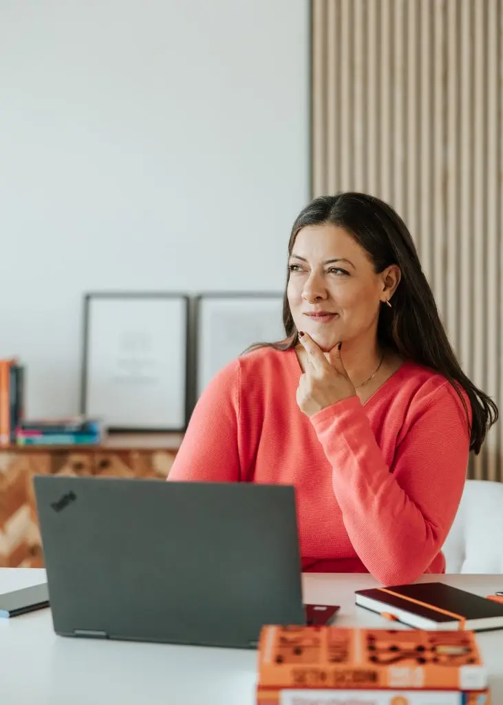 Healthcare PR Beratung. Frau in orangenen Pullover vor einem Laptop.